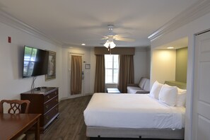 A hotel room with a bed, a desk, a chair, a television, and a ceiling fan.