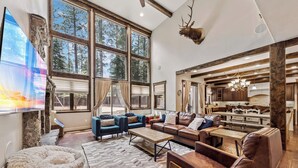 A spacious living room with large windows, a fireplace, and a kitchen area.