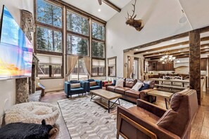 A spacious living room with large windows, a fireplace, and a kitchen area.