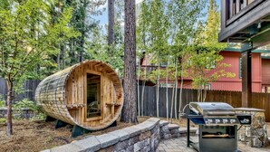 A wooden barrel structure, a stone wall, and a barbecue grill in a backyard setting.
