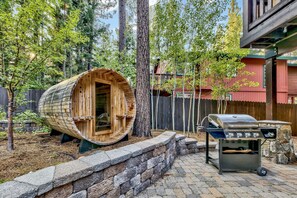 A wooden barrel structure, a stone wall, and a barbecue grill in a backyard setting.