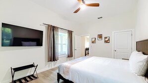 A bedroom with a bed, a ceiling fan, a TV mounted on the wall, and a window with curtains. - Rainbow River Oasis With Private Dock (Dunnellon)
