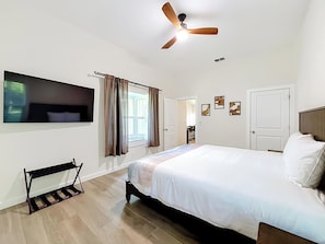 A bedroom with a bed, a ceiling fan, a TV mounted on the wall, and a window with curtains. - Rainbow River Oasis With Private Dock (Dunnellon)
