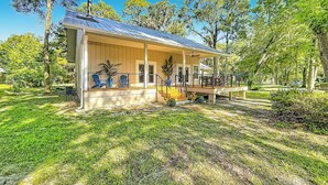 A single-story building with a covered porch and a small deck, surrounded by a well-maintained lawn and trees. - Rainbow River Oasis With Private Dock (Dunnellon)