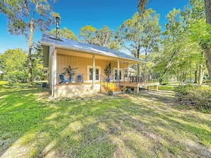 A single-story building with a covered porch and a small deck, surrounded by a well-maintained lawn and trees. - Rainbow River Oasis With Private Dock (Dunnellon)