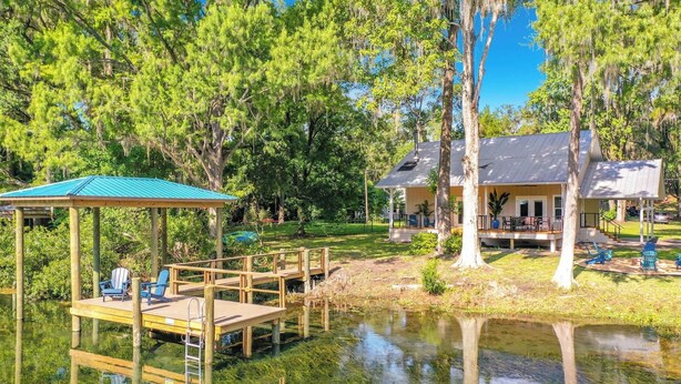 A lakeside property with a wooden dock, a covered seating area, and a house with a porch. - Rainbow River Oasis With Private Dock (Dunnellon)