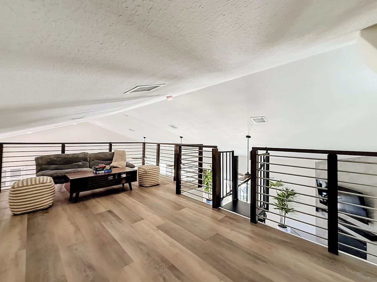 Ein geräumiges Loft mit hoher Decke, Holzboden, einer Sofagarnitur, einem Couchtisch und einem Geländer mit Blick.