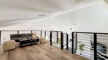 Ein geräumiges Loft mit hoher Decke, Holzboden, einer Sofagarnitur, einem Couchtisch und einem Geländer mit Blick.