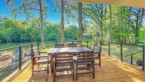 An outdoor deck with a table and chairs, overlooking a natural landscape with trees and a body of water. - Rainbow River Oasis With Private Dock (Dunnellon)