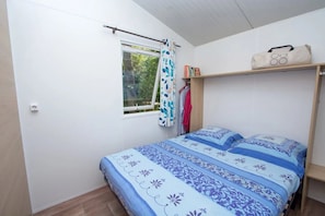 Ein Schlafzimmer mit einem Bett, einem Fenster mit Vorhang, einem Regal mit einer Tasche und einem Kleiderschrank.