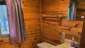 A wooden cabin bathroom with a toilet, sink, and shower curtain.