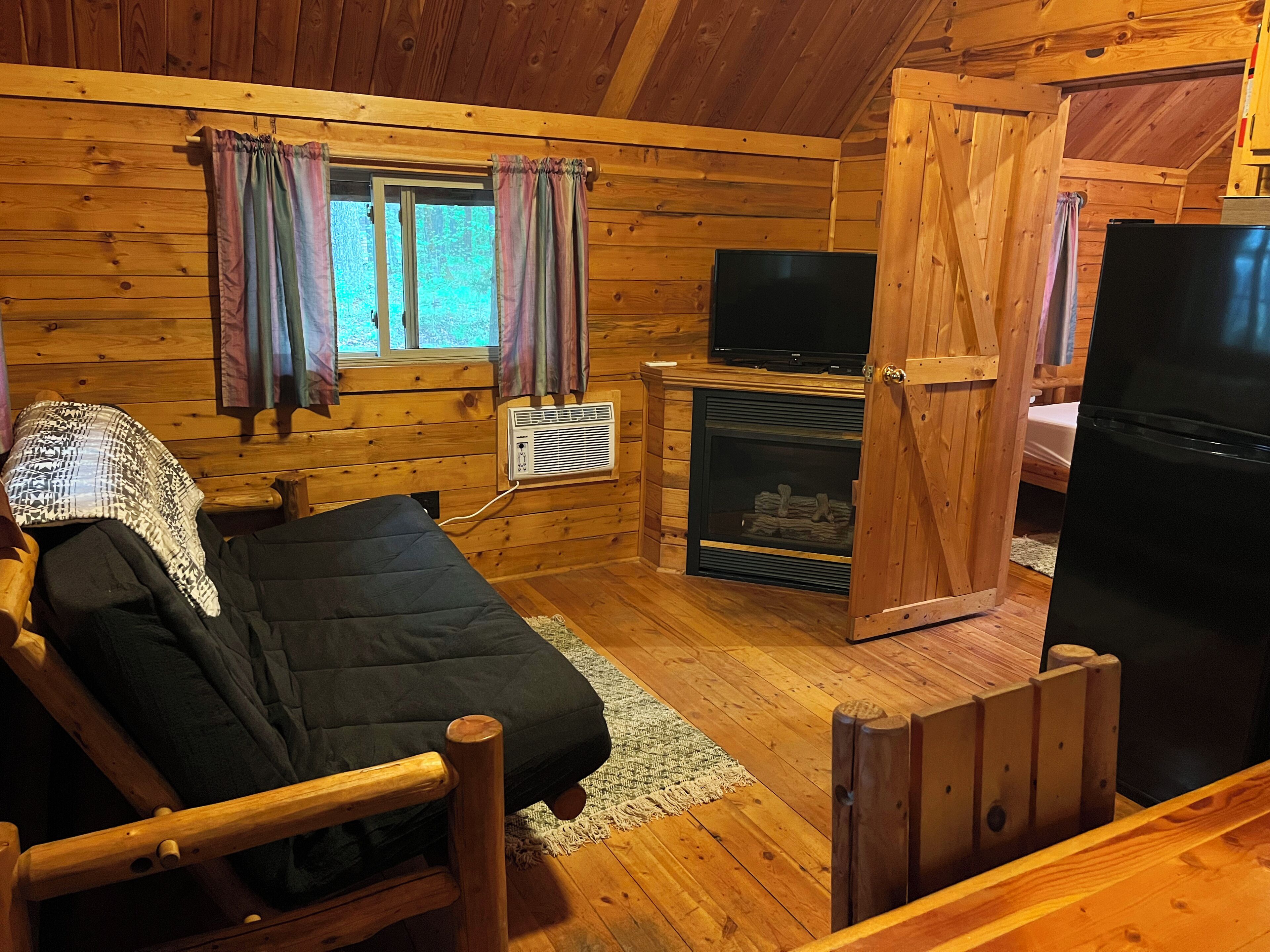 Une chambre de style rustique avec un lit, une télévision, une cheminée et un réfrigérateur.