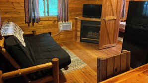 A log cabin room with a bed, a television, a fireplace, and a refrigerator.