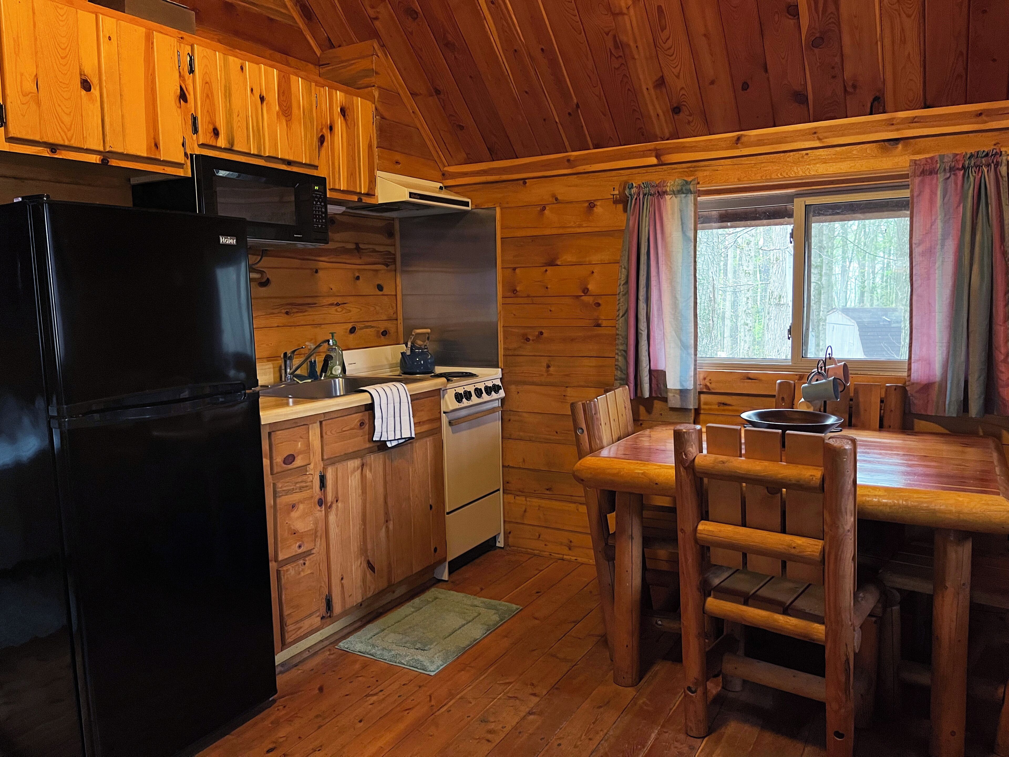 Une cuisine rustique, située dans une cabane en bois, équipée d’un réfrigérateur, d’une cuisinière et de meubles de rangement en bois.