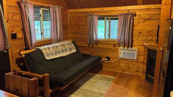 L’intérieur d’un chalet en bois, avec un canapé, deux fenêtres avec des rideaux, une cheminée et un plancher en bois.