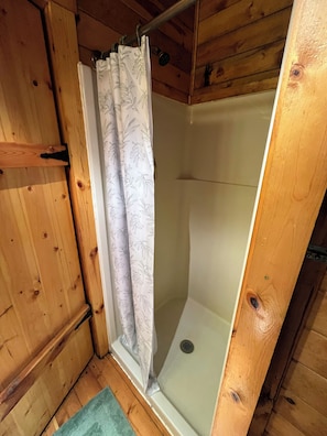 A wooden cabin with a shower area, wooden walls, and a metal door.