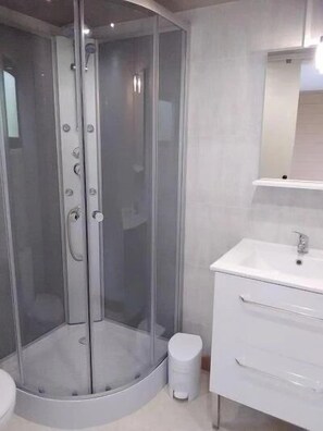 Une salle de bain moderne avec une douche à parois de verre, un lavabo blanc et un miroir au-dessus du meuble-lavabo.