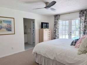 Ein Schlafzimmer mit Bett, Deckenventilator, Kommode, Fernseher und einem Fenster mit Vorhängen.