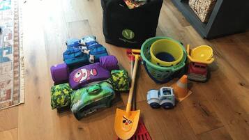 A room with a wooden floor, a black bag with a logo, a green and yellow basket, a toy truck, and several colorful cushions.