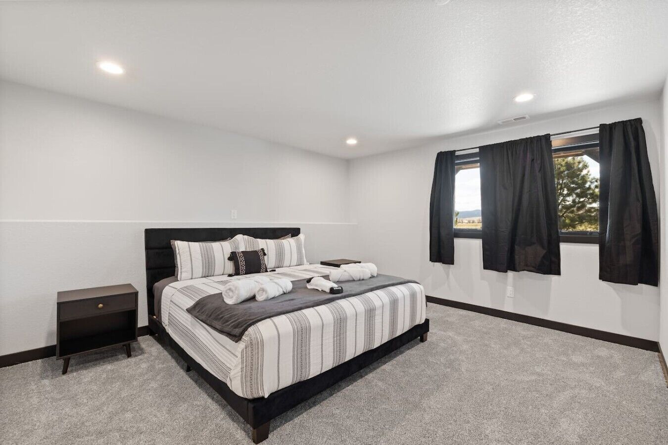 A bedroom with a bed, a nightstand, a window with curtains, and a view outside.