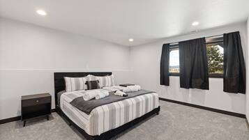 A bedroom with a bed, a nightstand, a window with curtains, and a view outside.