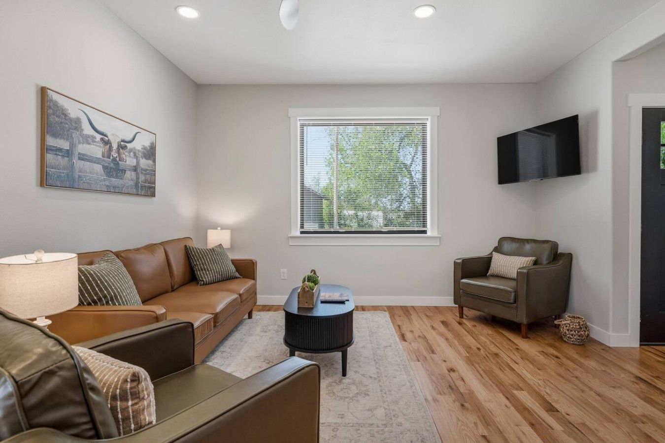 A living room with a brown leather sofa, a smaller sofa, a coffee table, and a TV mounted on the wall.