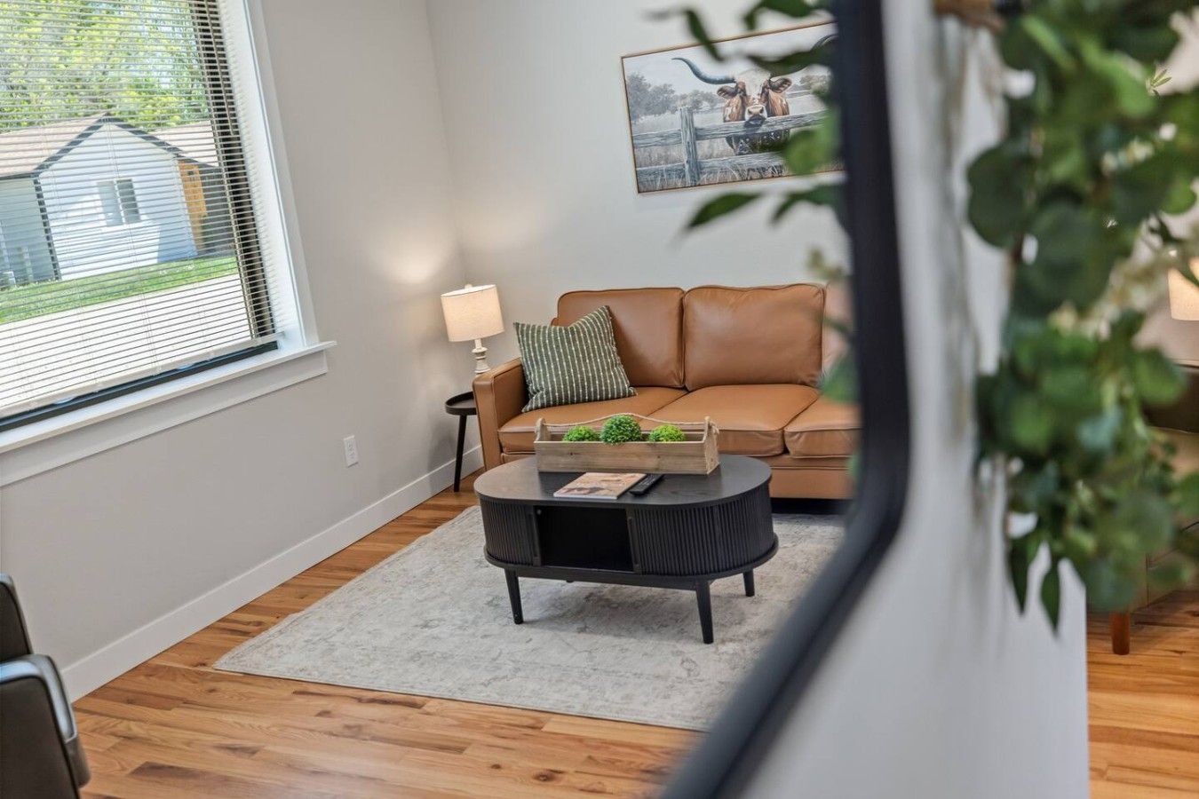 A living room with a brown leather sofa, a round coffee table with a tray, a lamp, and a framed picture on the wall.
