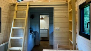 A cabin interior with a wooden interior, a kitchen area, a bathroom, and a window with a view of greenery. - Cabane 3 étoiles - ccbeche (Neuilly-sur-Marne)