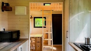 A compact kitchen with wooden cabinets, a microwave, a stove, and a window with a view of greenery. - Cabane 3 étoiles - ccbeche (Neuilly-sur-Marne)