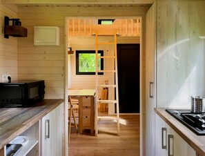 A compact kitchen with wooden cabinets, a microwave, a stove, and a window with a view of greenery.