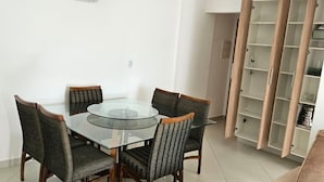 A dining area with a glass table and chairs, a beige sofa, and a built-in wooden shelving unit. - Family Apartment with 2 Bedrooms in the City Center, 200m from the Beach, Furnished and with AC (Praia Grande)