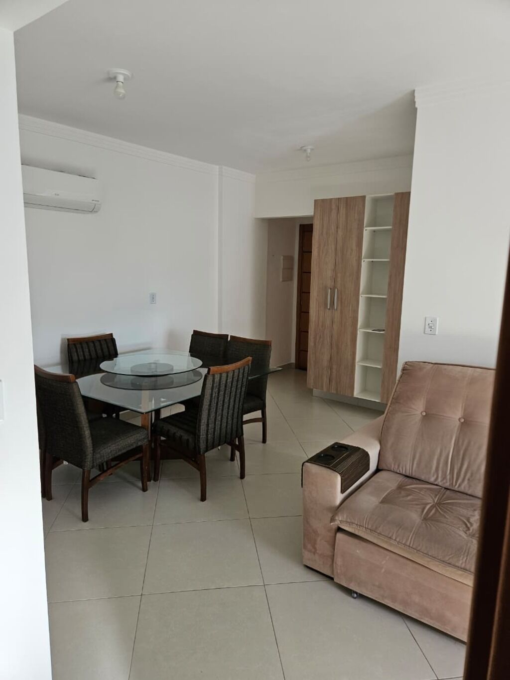 A dining area with a glass table and chairs, a sofa, and a wooden cabinet with shelves.