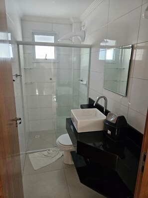 Une salle de bain avec une douche à parois de verre, des toilettes blanches, un lavabo noir et un miroir.