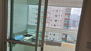 A room with a sliding glass door leading to a balcony with a view of apartment buildings. - Family Apartment with 2 Bedrooms in the City Center, 200m from the Beach, Furnished and with AC (Praia Grande)