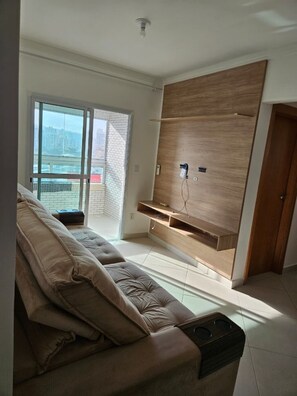 Een woonkamer met een bank, een houten tv-meubel en een schuifdeur naar een balkon.