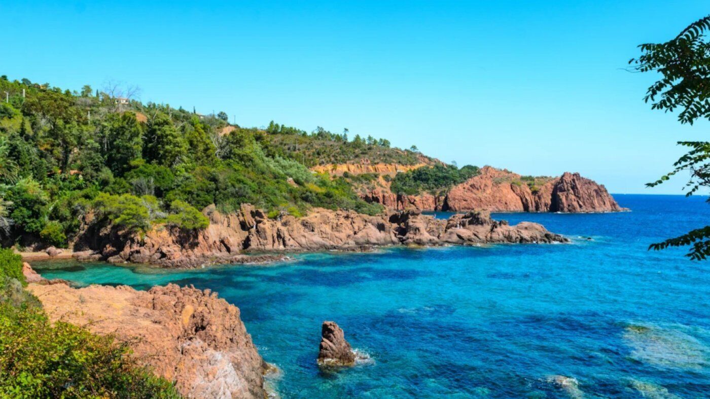 A coastal landscape with rocky cliffs, clear blue waters, and dense greenery.