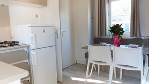Een kleine keuken met een witte koelkast, een gasfornuis en een eethoek met witte stoelen en een tafel.
