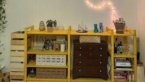 Ein Zimmer mit Holzboden, einer gelben Regaleinheit mit verschiedenen Gegenständen und einer Lichterkette, die eine Herzform an der Wand bildet.