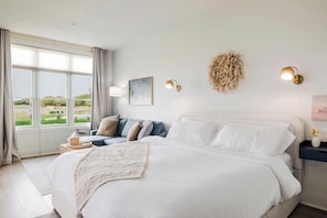 Ein Schlafzimmer mit einem großen Bett, einem Nachttisch mit Lampe, Blick ins Grüne und einem Wandbild.