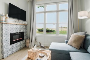 Ein Wohnzimmer mit Fernseher, Kamin und Blick ins Freie.