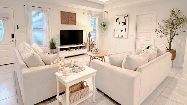 Een woonkamer met een witte bank, een bijzettafeltje, een televisie en een potplant.