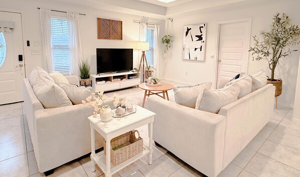 Ein Wohnzimmer mit einem weiĂen Sofa, einem Couchtisch, einem Fernseher und einer Zimmerpflanze.