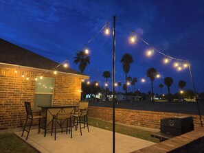 An outdoor patio with a brick wall, a grill, and string lights.