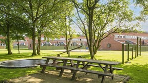 A picnic table in a park with a trampoline, trees, and a playground in the background. - 4 Person Holiday Park Home in Hemmet (Hemmet)