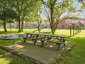 Ein Picknicktisch in einem Park mit Trampolin, Bäumen und einem Spielplatz im Hintergrund.
