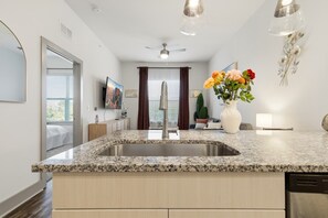 A modern kitchen with granite countertops, a stainless steel sink, a ceiling fan, and a large window with curtains. - Cozy 1-bedroom apartment near FIFA, universal studio resort in tranquil Frisco (Frisco)