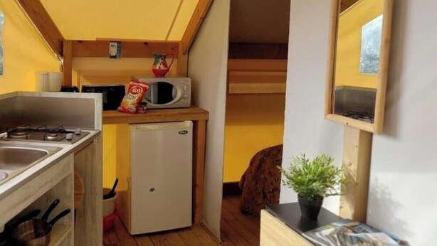 Una cocina compacta con microondas, un refrigerador pequeño y un lavamanos. Tiene techo de madera y una ventana.