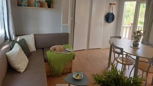A living room with a sofa, a small table, a dining table, and a door. - Camping 3 étoiles - Piscine  - ccbfidi (Les Moutiers-en-Retz)
