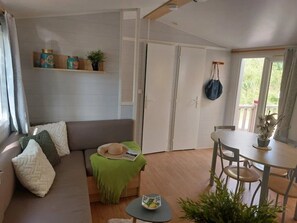A living room with a sofa, a small table, a dining table, and a door. - Camping 3 étoiles - Piscine  - ccbfidi (Les Moutiers-en-Retz)