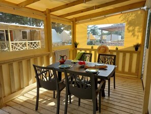 A covered outdoor dining area with a table set for four, surrounded by chairs. - Camping 3 étoiles - Piscine  - ccbfidi (Les Moutiers-en-Retz)